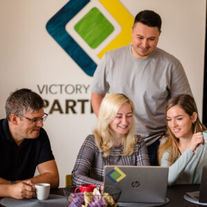 Four Victory Square Partners employees gathered around a computer, having a pleasant time working,